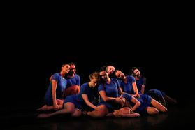 Group of dancers in blue costumes grouped in pose on the floor